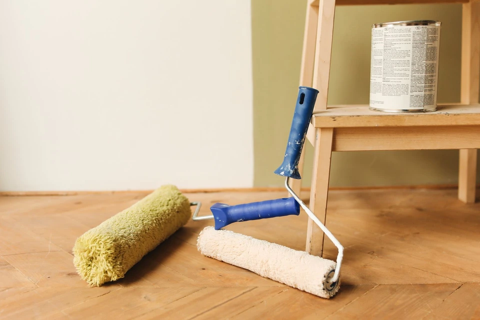 Deux rouleaux de peinture posés sur un parquet au pied d'un tabouret